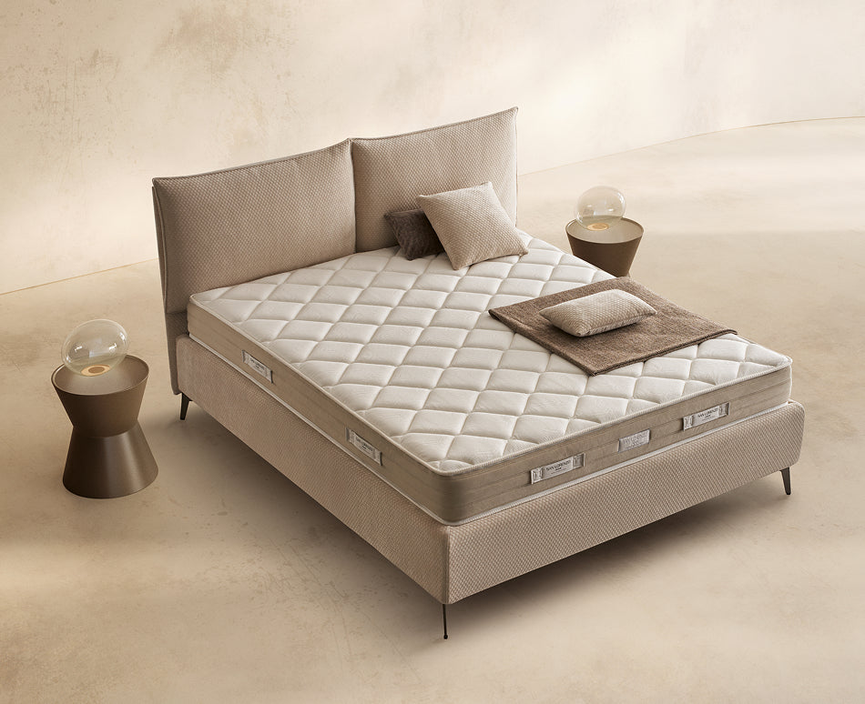 Materasso Memory Sleep posizionato su un letto in ambiente neutro con sopra cuscini e scaldapiedi warmie