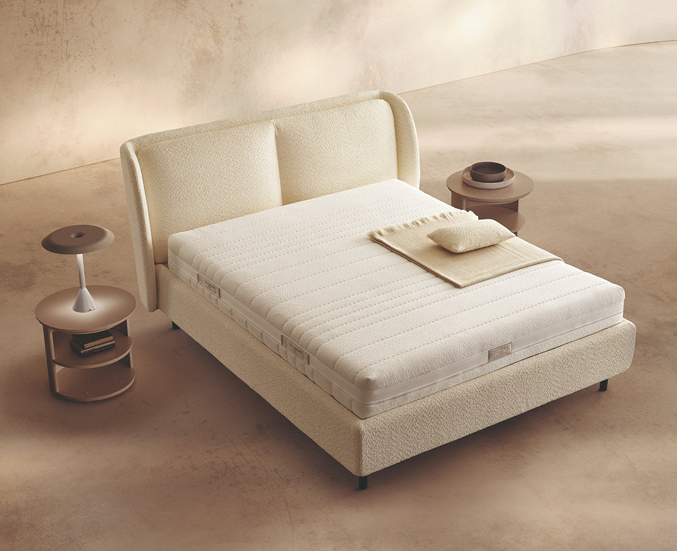 Materasso Memory Touch Evolution posizionato su un letto in ambiente neutro con sopra cuscini e scaldapiedi warmie