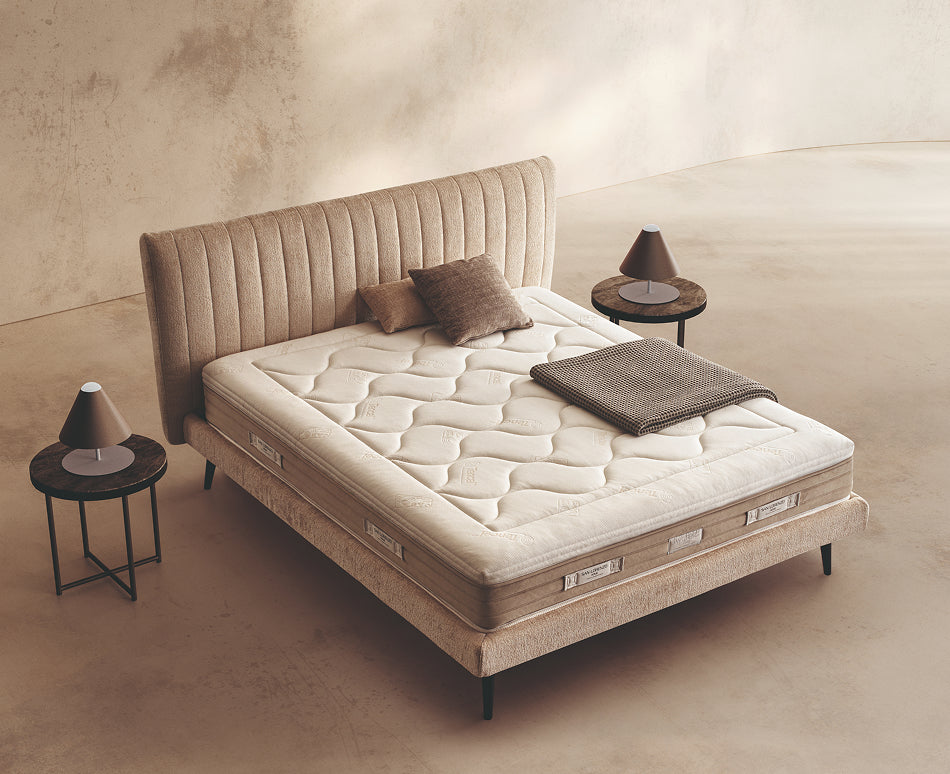 Materasso Platinum Fresh posizionato su un letto in ambiente neutro con sopra cuscini e scaldapiedi warmie
