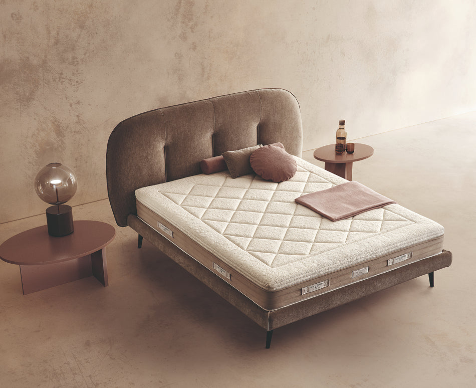 Materasso Royal Fresh posizionato su un letto in ambiente neutro con sopra cuscini e scaldapiedi warmie