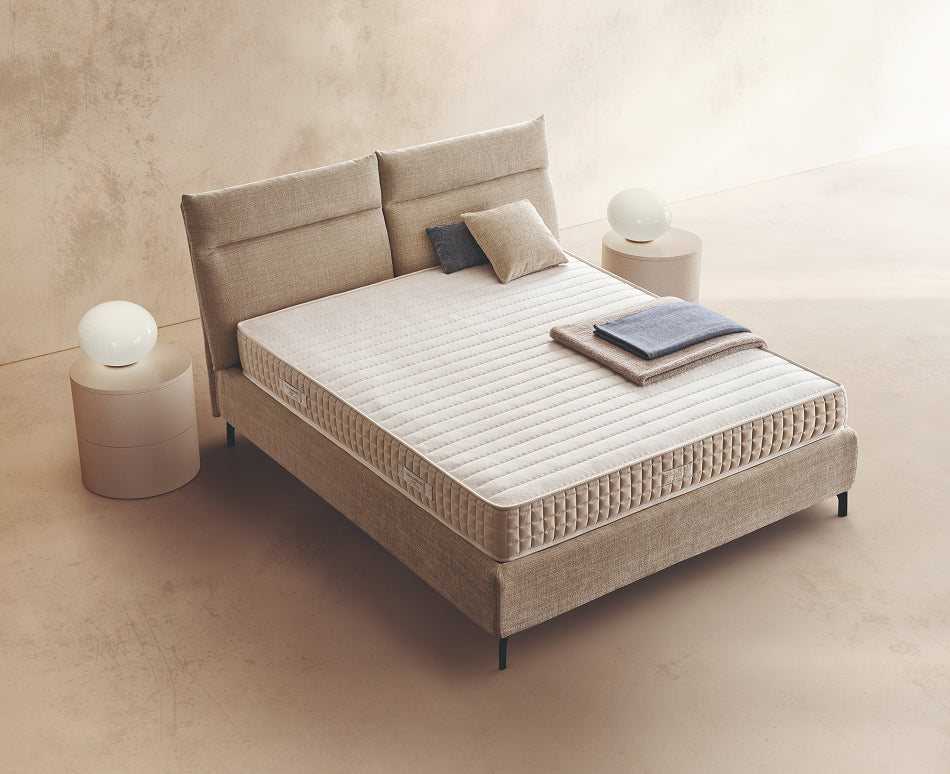 Materasso Amber posizionato su un letto in ambiente neutro con sopra cuscini e scaldapiedi warmie