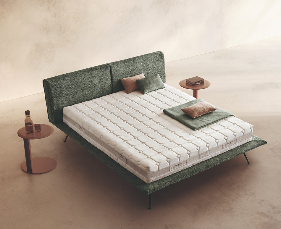 Materasso Cashmere Comfort posizionato su un letto in ambiente neutro con sopra cuscini e scaldapiedi warmie