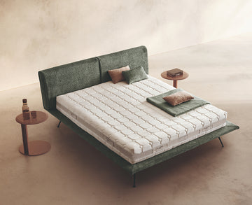 Materasso Cashmere Comfort posizionato su un letto in ambiente neutro con sopra cuscini e scaldapiedi warmie