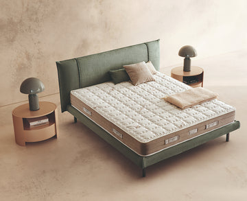 Materasso Harmony Fresh posizionato su un letto in ambiente neutro con sopra cuscini e scaldapiedi warmie