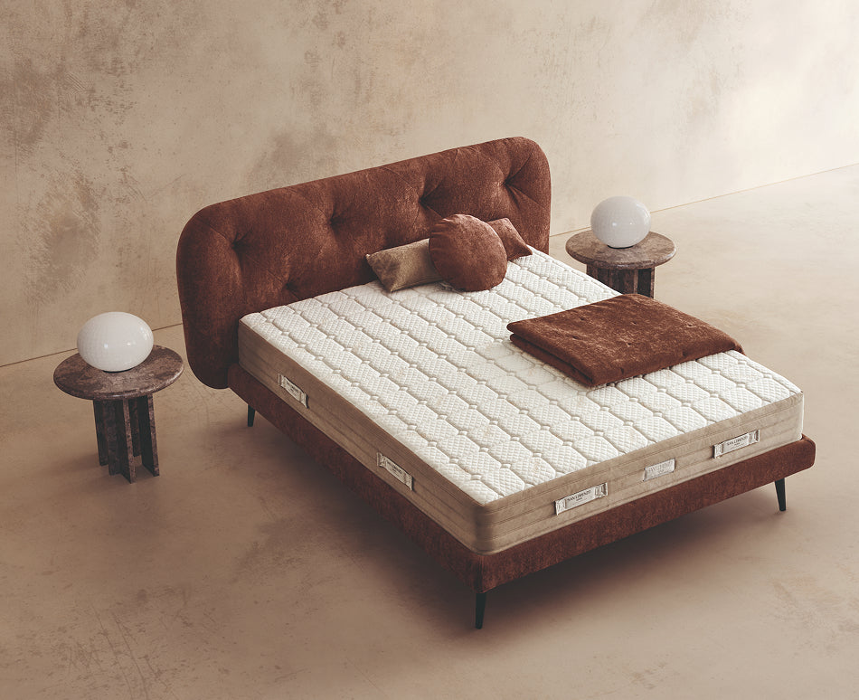 Materasso Idra Fresh posizionato su un letto in ambiente neutro con sopra cuscini e scaldapiedi warmie