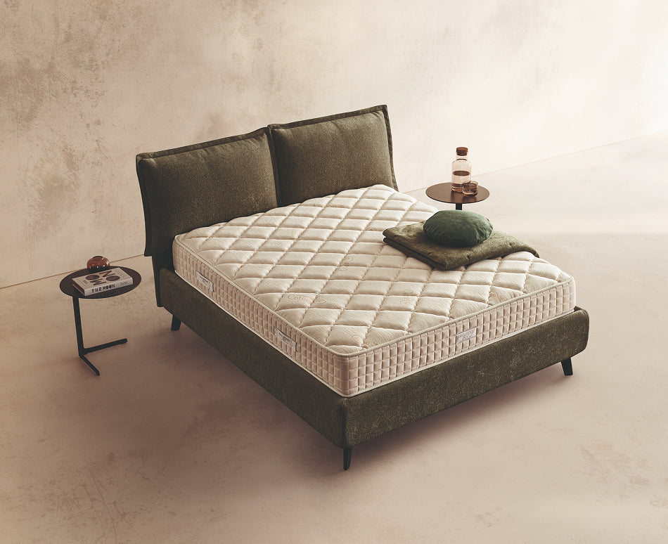 Materasso Incanto Memory posizionato su un letto in ambiente neutro con sopra cuscini e scaldapiedi warmie