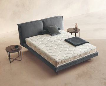 Materasso Memory First posizionato su un letto in ambiente neutro con sopra cuscini e scaldapiedi warmie