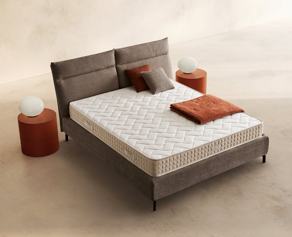 Materasso Noor posizionato su un letto in ambiente neutro con sopra cuscini e scaldapiedi warmie