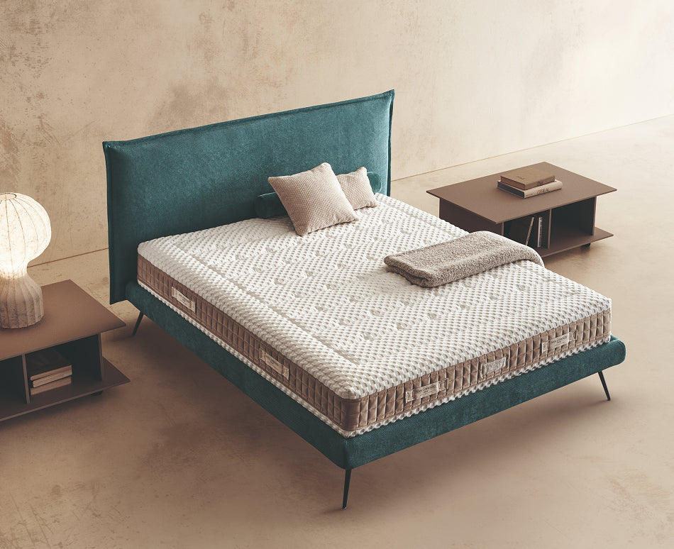 Materasso Orthoease posizionato su un letto in ambiente neutro con sopra cuscini e scaldapiedi warmie