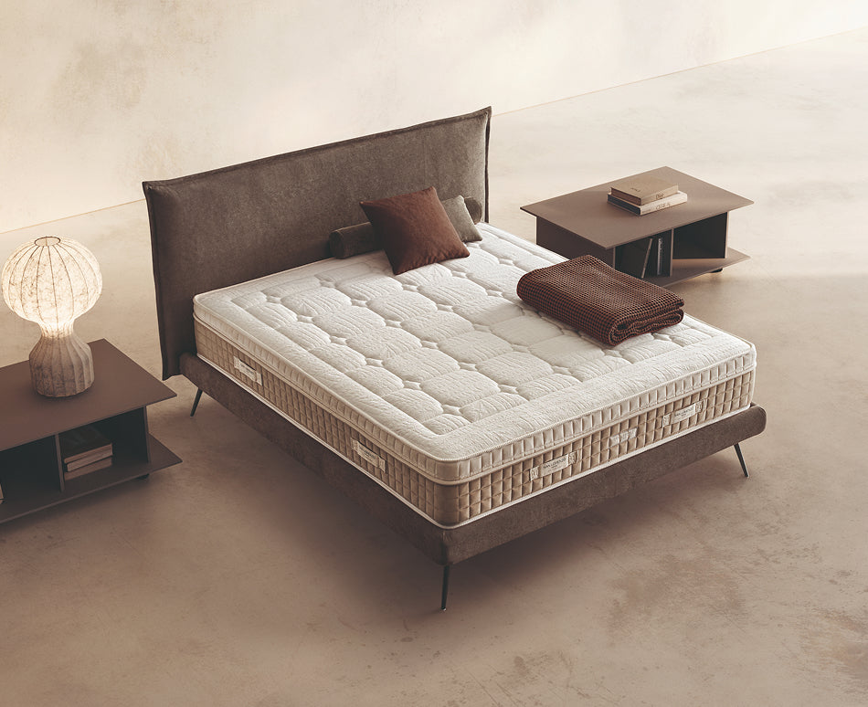 Materasso Pocket Foam posizionato su un letto in ambiente neutro con sopra cuscini e scaldapiedi warmie