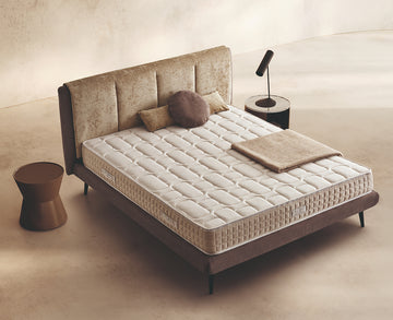 Materasso Regard posizionato su un letto in ambiente neutro con sopra cuscini e scaldapiedi warmie