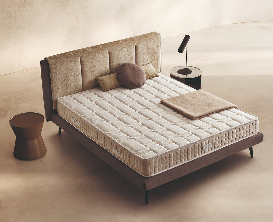 Materasso Regard posizionato su un letto in ambiente neutro con sopra cuscini e scaldapiedi warmie