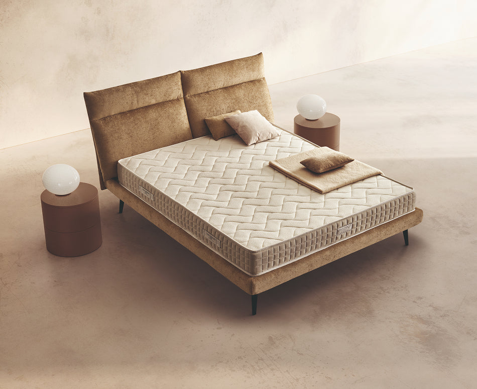 Materasso Relax posizionato su un letto in ambiente neutro con sopra cuscini e scaldapiedi warmie