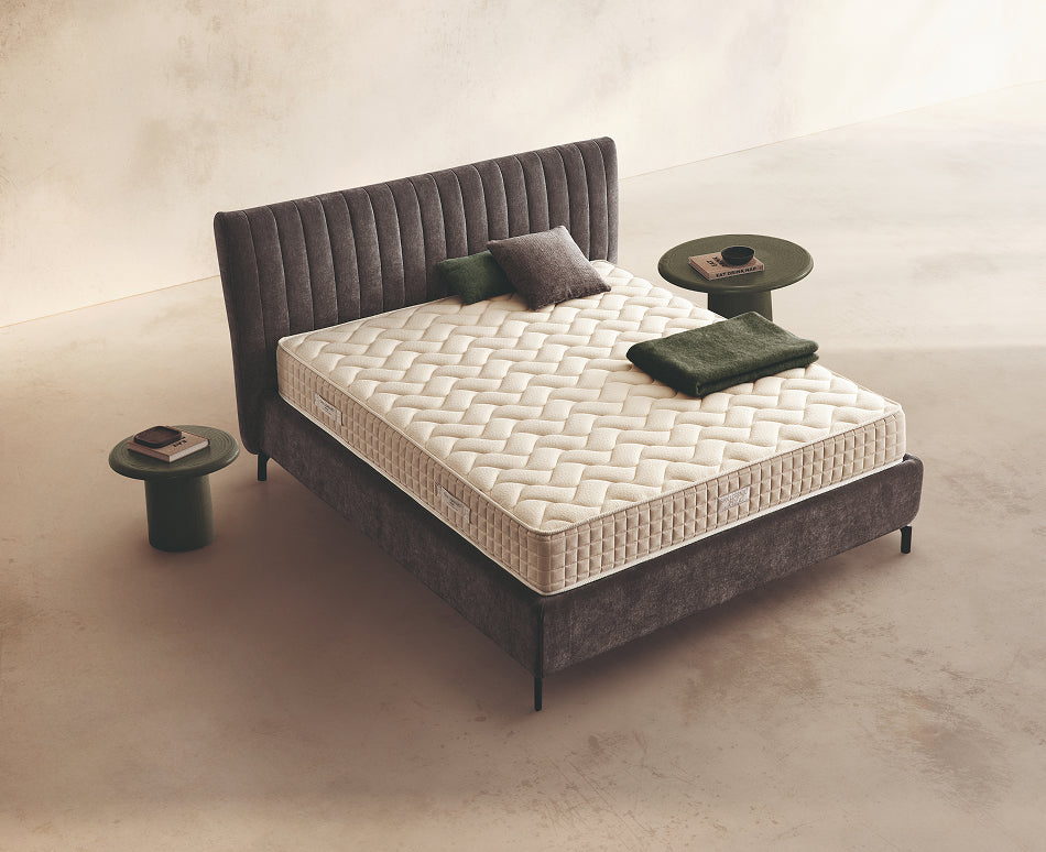 Materasso Relax Plus Mind posizionato su un letto in ambiente neutro con sopra cuscini e scaldapiedi warmie