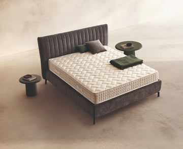 Materasso Relax Plus Mind posizionato su un letto in ambiente neutro con sopra cuscini e scaldapiedi warmie