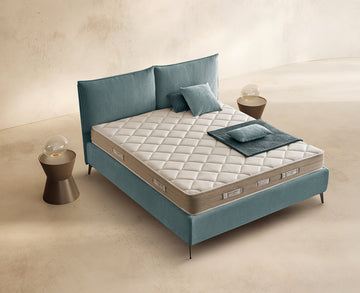 Materasso Sleep Fresh posizionato su un letto in ambiente neutro con sopra cuscini e scaldapiedi warmie