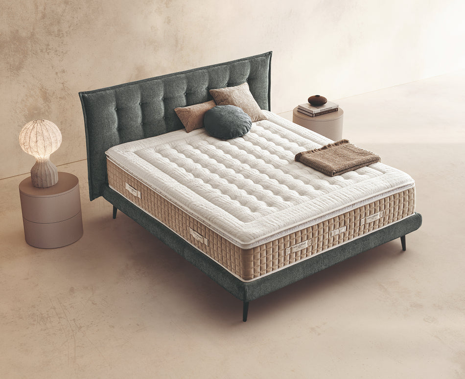 Materasso Super Topper Mind posizionato su un letto in ambiente neutro con sopra cuscini e scaldapiedi warmie