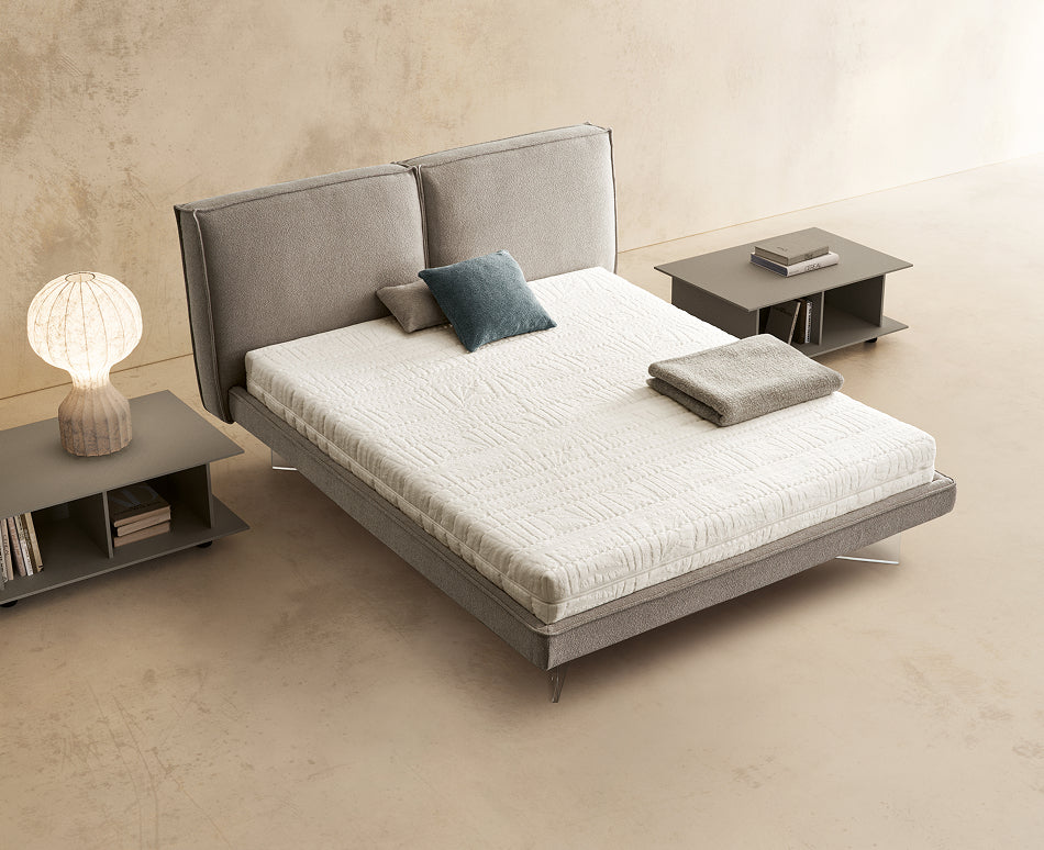Materasso White Bed posizionato su un letto in ambiente neutro con sopra cuscini e scaldapiedi warmie