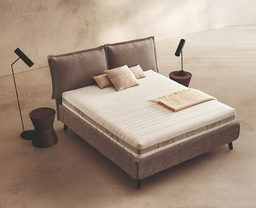 Materasso Aloe Mind Comfort posizionato su un letto in ambiente neutro con sopra cuscini e scaldapiedi warmie